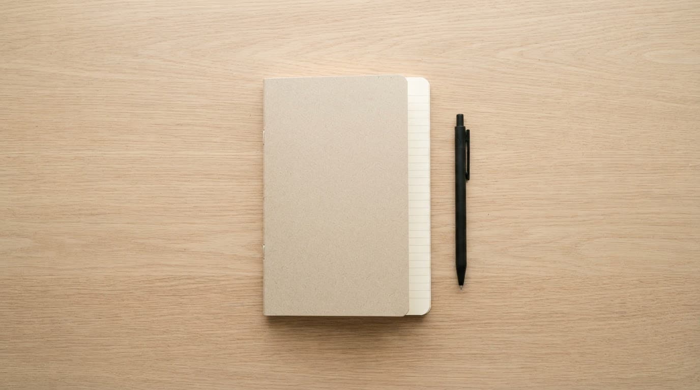 A notebook and pen on a light wooden desk.